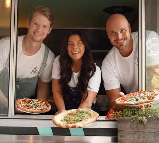 Bild som visar tre glada personer som håller ut pizza från pizzatrucken Mowgliz.