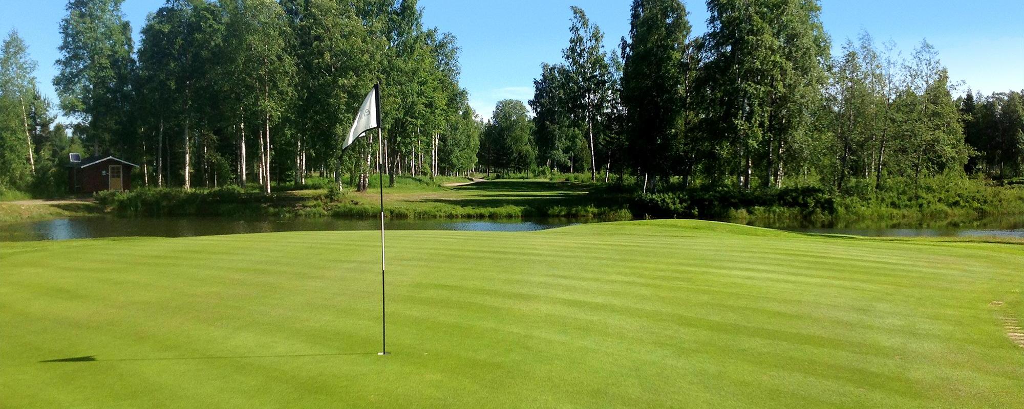 En finklippt grön green. Mitt på står en flagga som viftar i den svaga vinden. Himlen är blå och solen lyser.