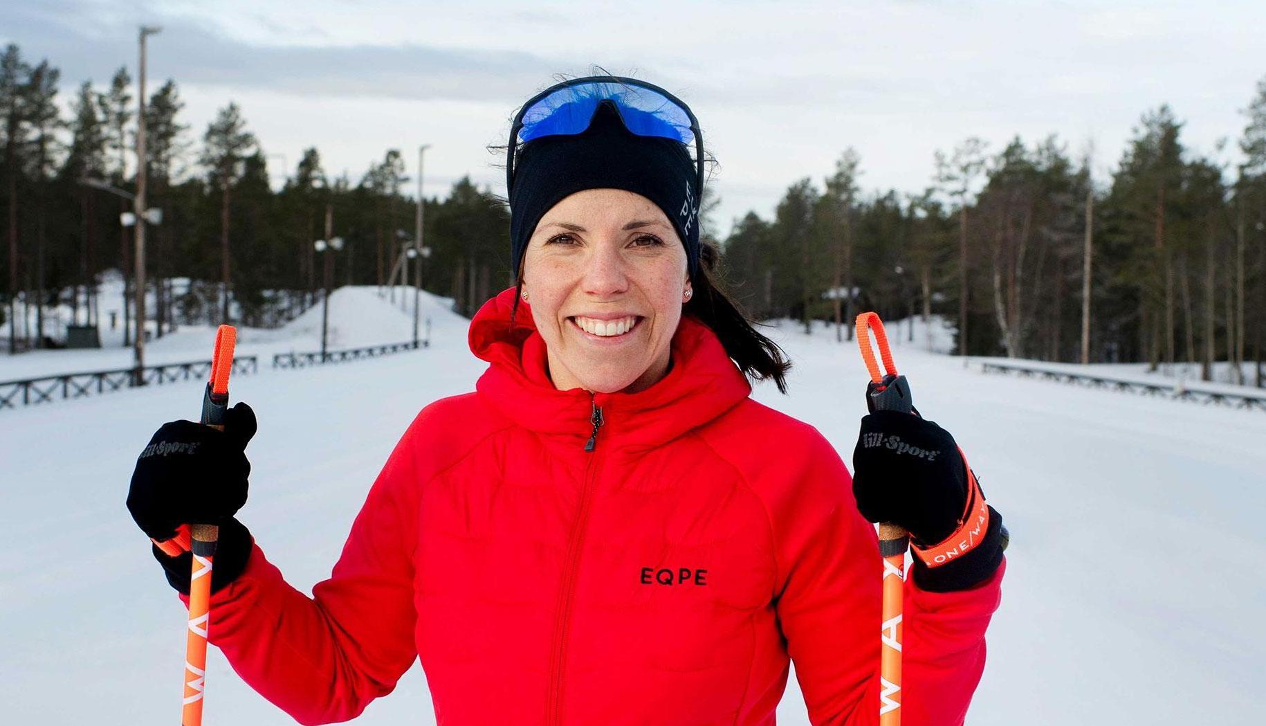 Fotografi av Charlotte Kalla som sår i ett skidspår. Hon håller i stavar i varsin hand, har röd jacka och skidglasögon på huvudet
