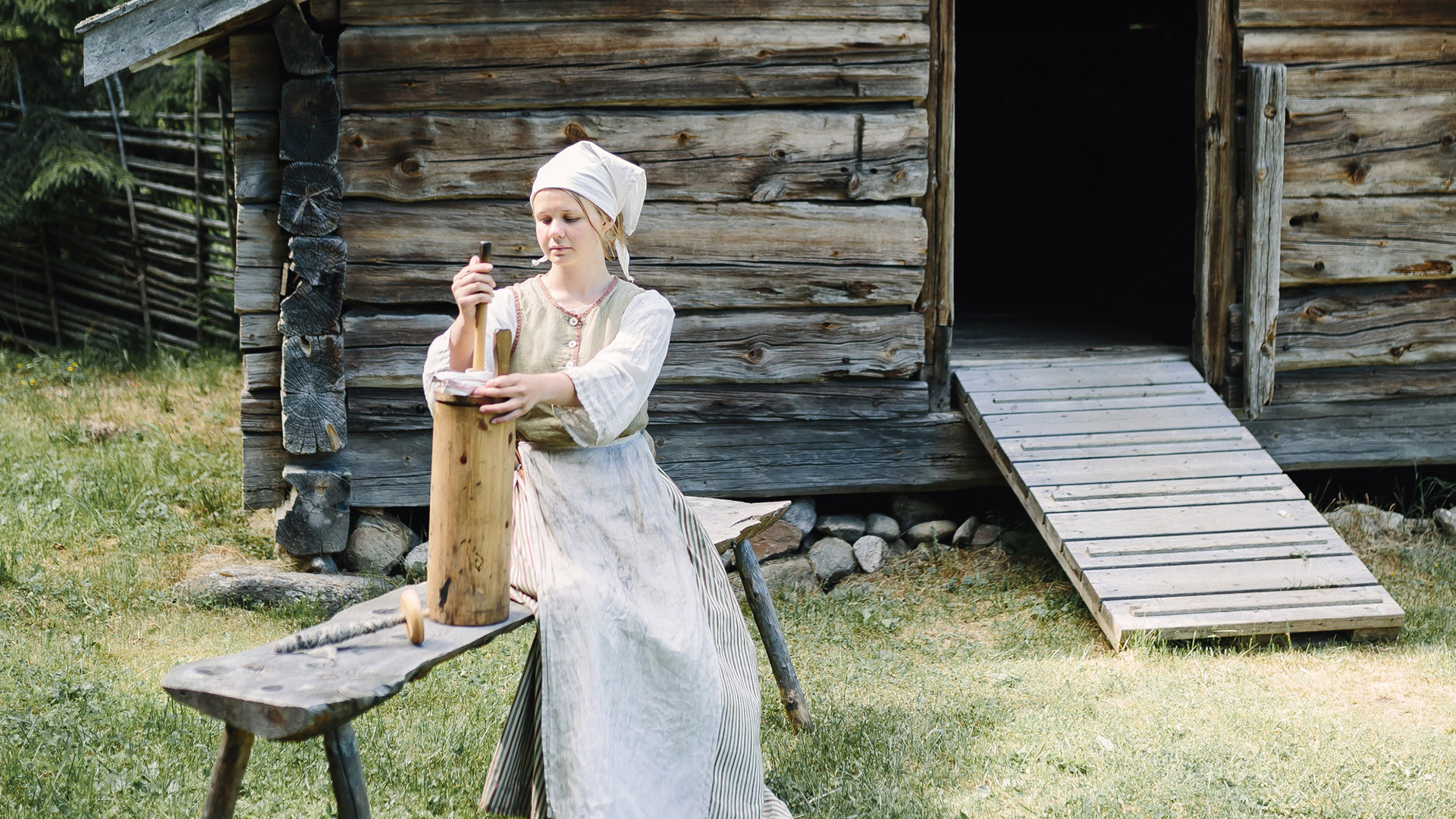 Fäbodstinta kärnar smör utanför äldre byggnad. Foto: Norra Berget.