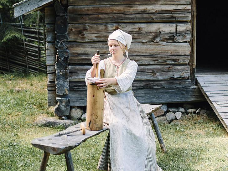 Fäbodstinta kärnar smör utanför äldre byggnad. Foto: Norra Berget.