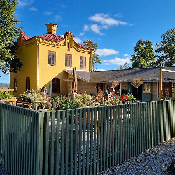 Gul anrik byggnad med inhägnad trädgård framför.