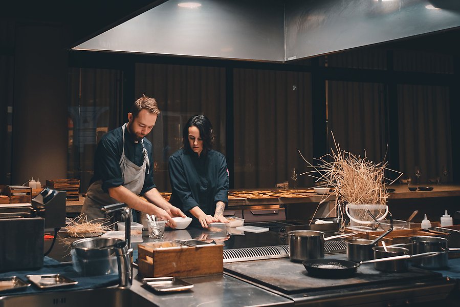 Man och kvinna står i restaurangkök och tillreder mat tillsammans.
