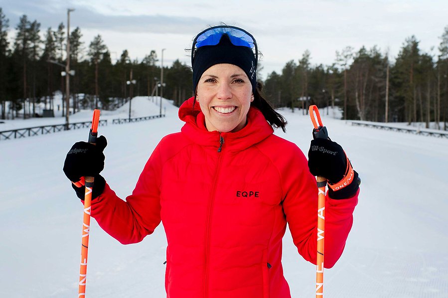 Fotografi av Charlotte Kalla som sår i ett skidspår. Hon håller i stavar i varsin hand, har röd jacka och skidglasögon på huvudet