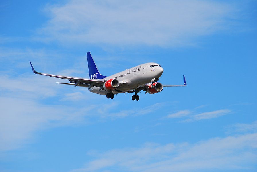 Ett stort vitt flygplan flyger i luften. Himlen är ljusblå med bara några få moln.